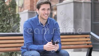 坐在长椅上听智能手机音乐的年轻人